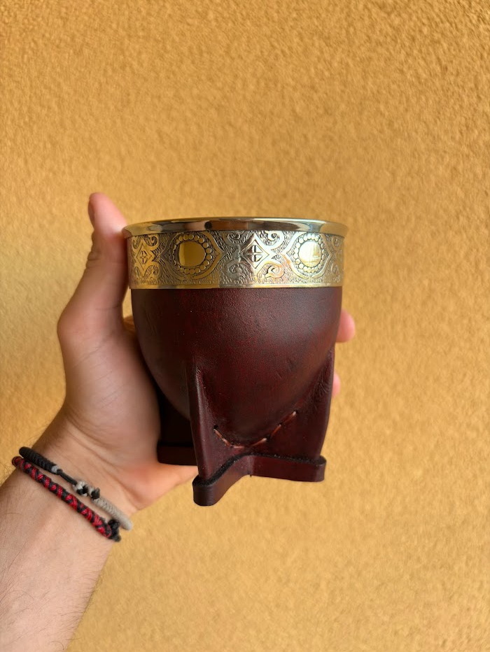 Mate imperial color vino con virola de alpaca decorada con motivos circulares, sostenido en una mano.