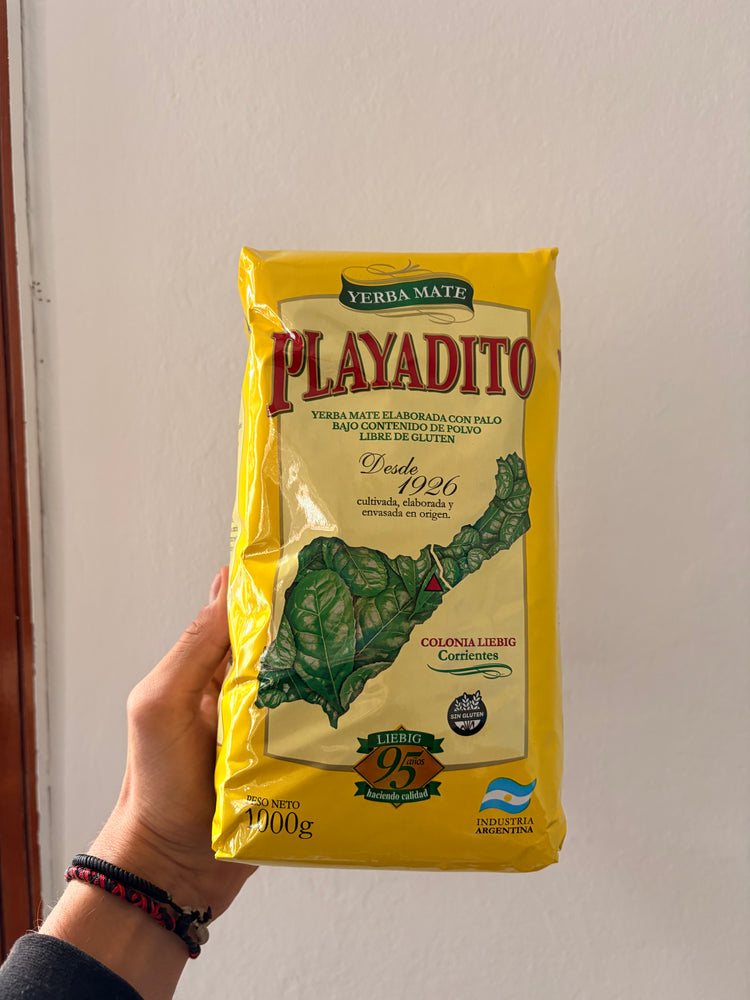 Paquete amarillo de yerba mate Playadito de 1 kg, sostenido en una mano.