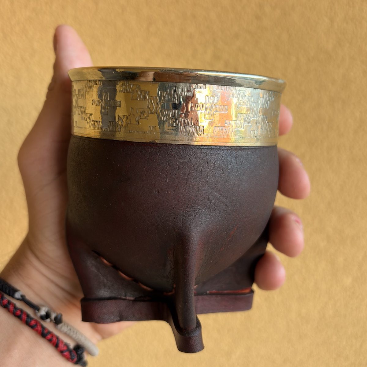 Mate imperial bordó con virola de alpaca de diseño geométrico, sostenido en una mano.