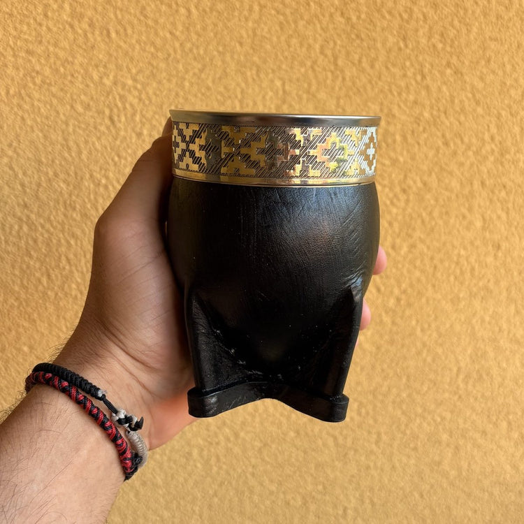 Mate imperial negro con virola de alpaca de diseño geométrico y base de cuero, sostenido en una mano.
