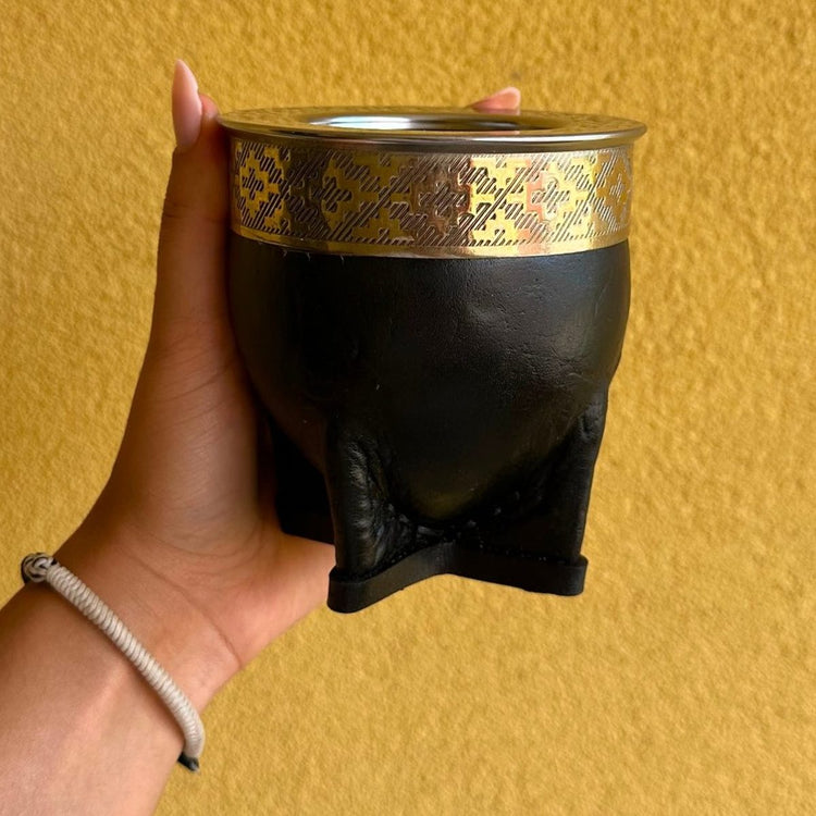 Mate imperial negro con virola de alpaca grabada, sostenido en una mano.