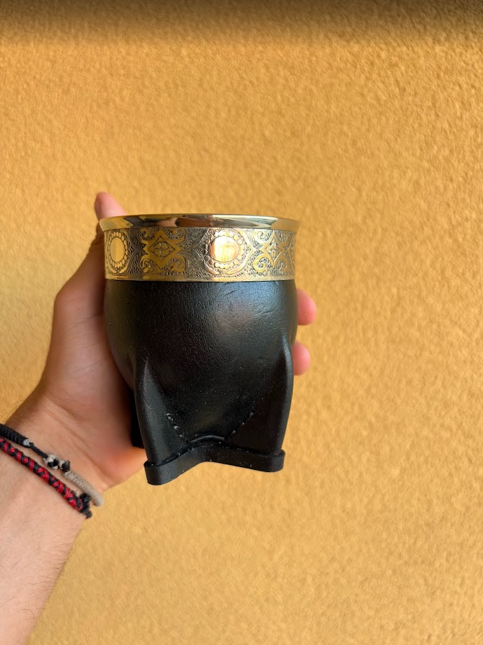 Mate imperial negro con virola de alpaca decorada con motivos circulares, sostenido en una mano.